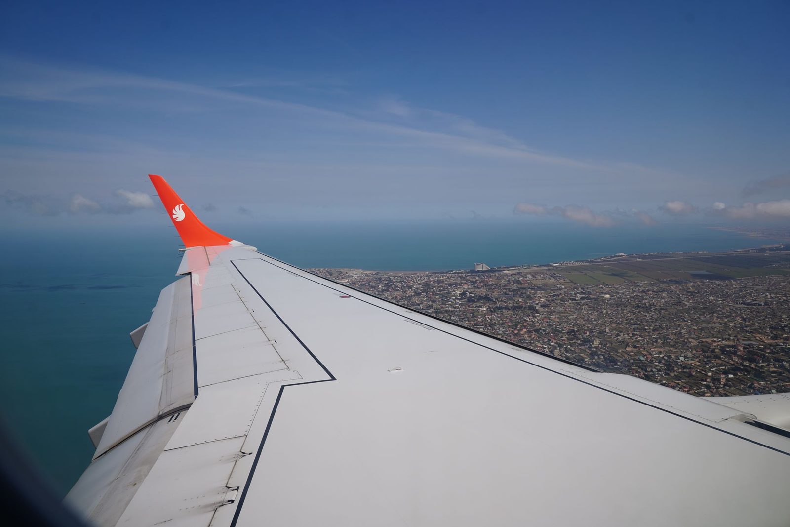 View of an aircraft wing over a coastline and the Aegean Sea from a passenger window
