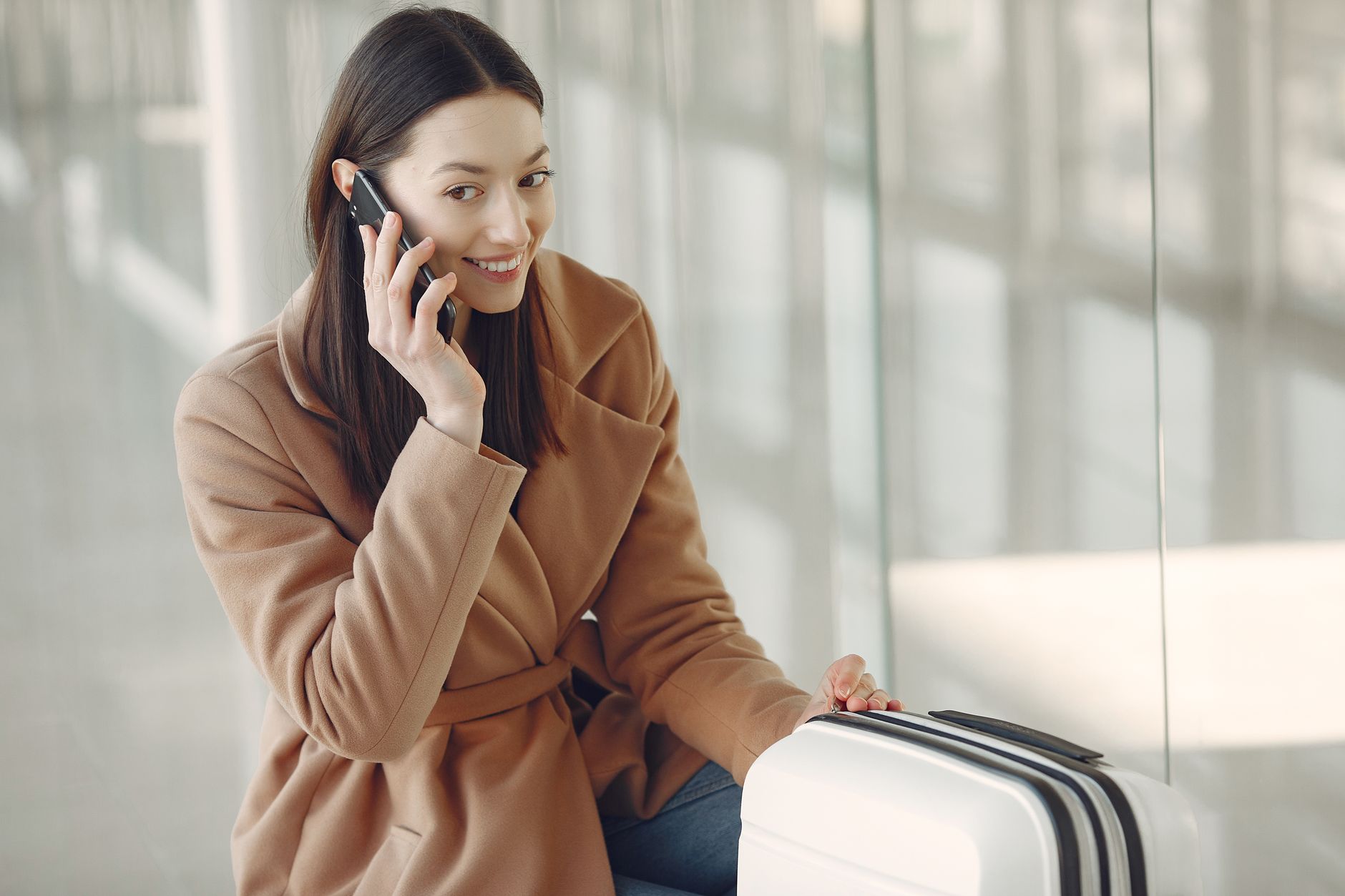 Traveller on a phone with a suitcase beside the terminal windows at Santorini Airport